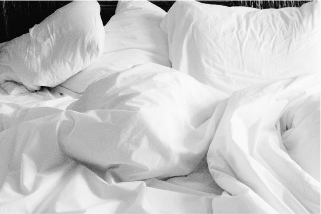 Ein Bett auf dem weisse Kopfkissen und Decken liegen