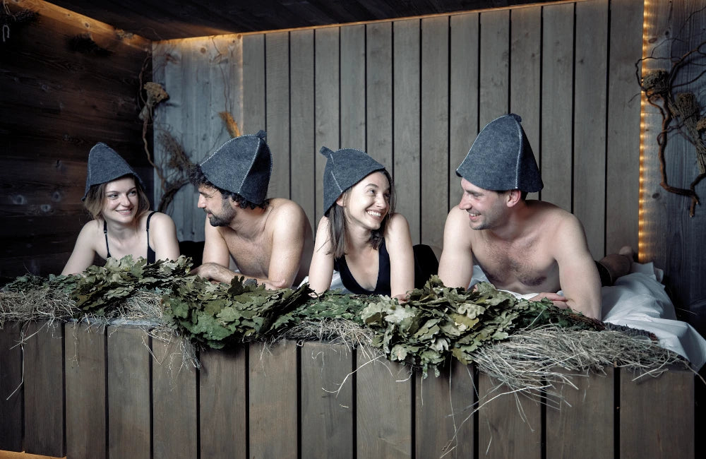 Vier Freunde liegen auf Kräutern in der Sauna mit Saunhut auf